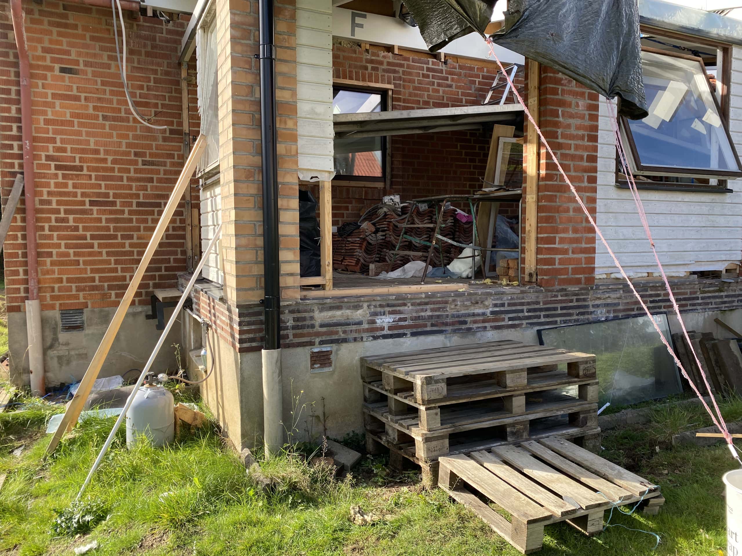 Tillfällig ingång under renovering med byggmaterial och pallställning.