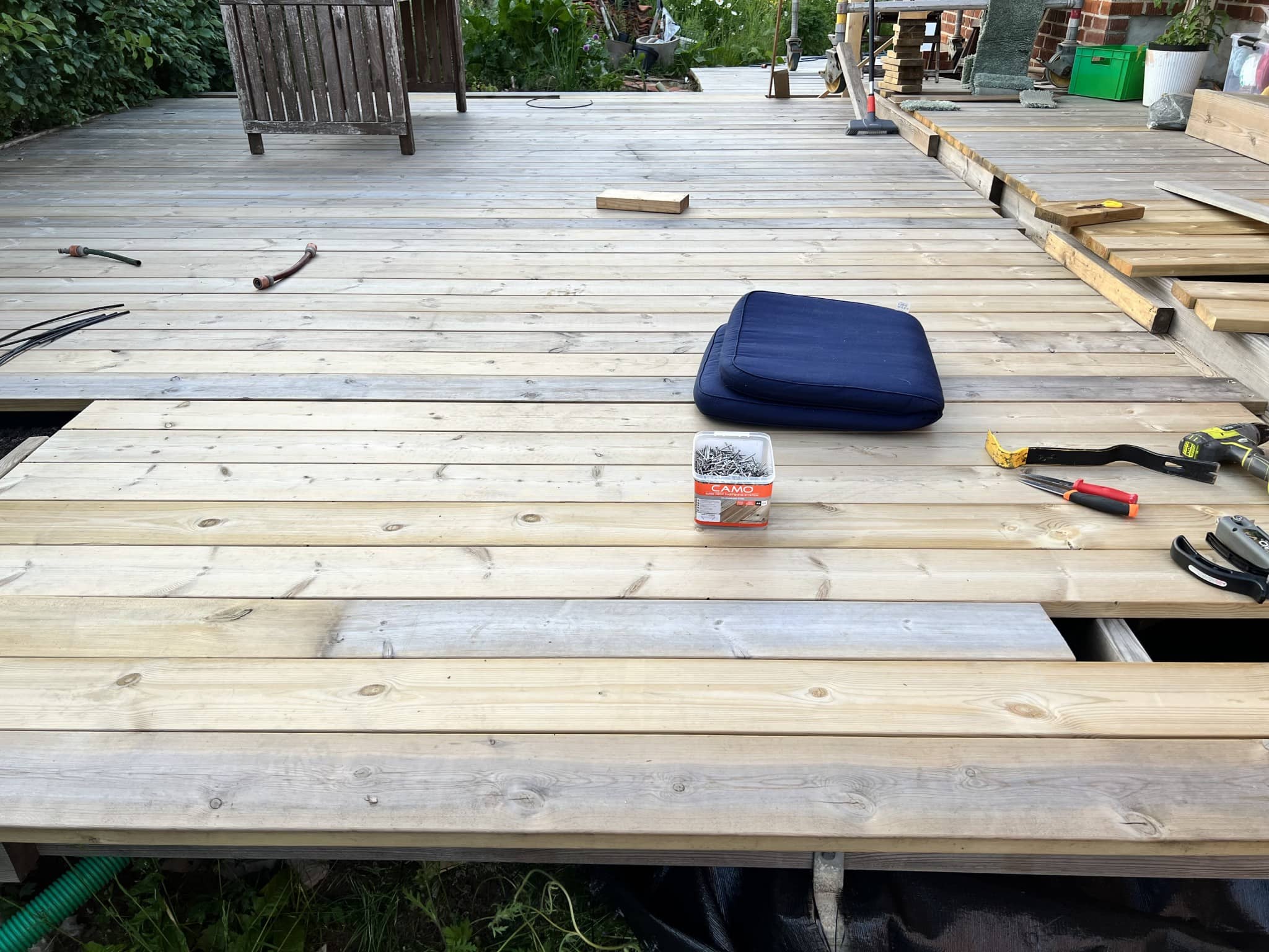 Nyrenoverad altan med träplankor, ett sittunderlag och verktyg synliga. En inbjudande utomhusmiljö som förbereds för avkoppling.