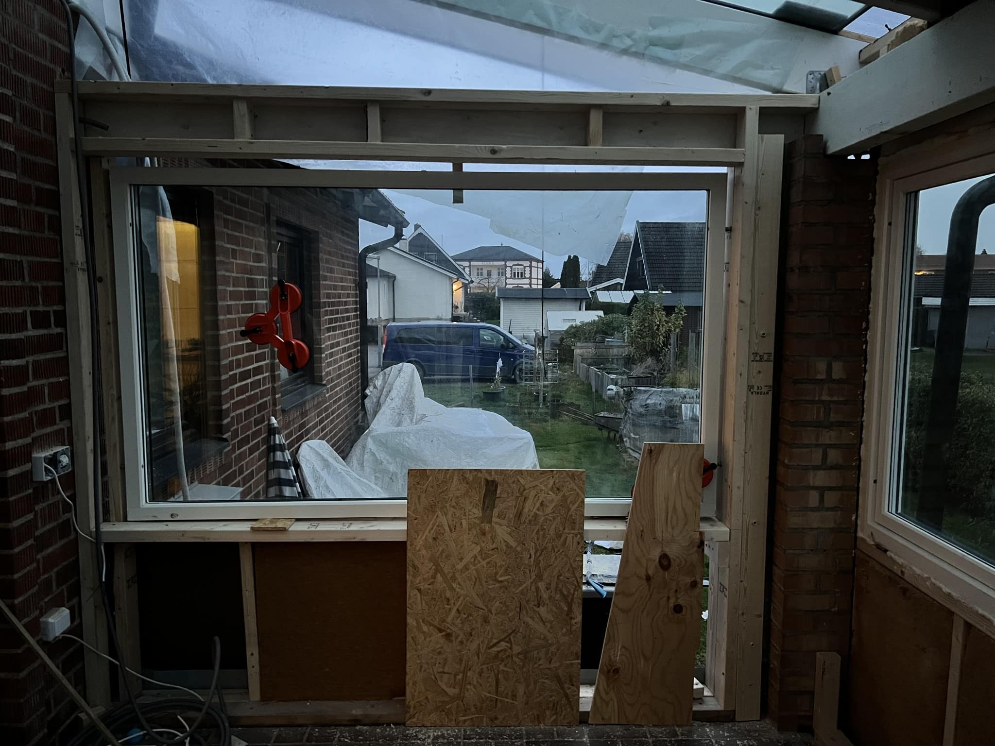 En pågående renovering av ett fönsterparti, med utsikt mot en trädgård och byggmaterial synligt inuti rummet.