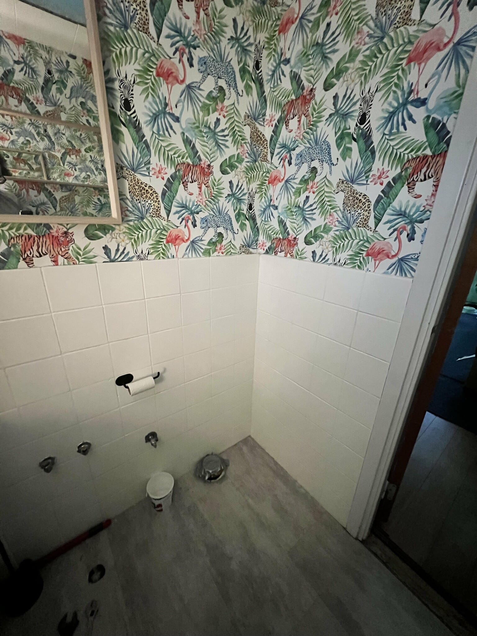 Badrum under renovering med livfull djungeltapet och vita kakelplattor. Verktyg och material syns på golvet.