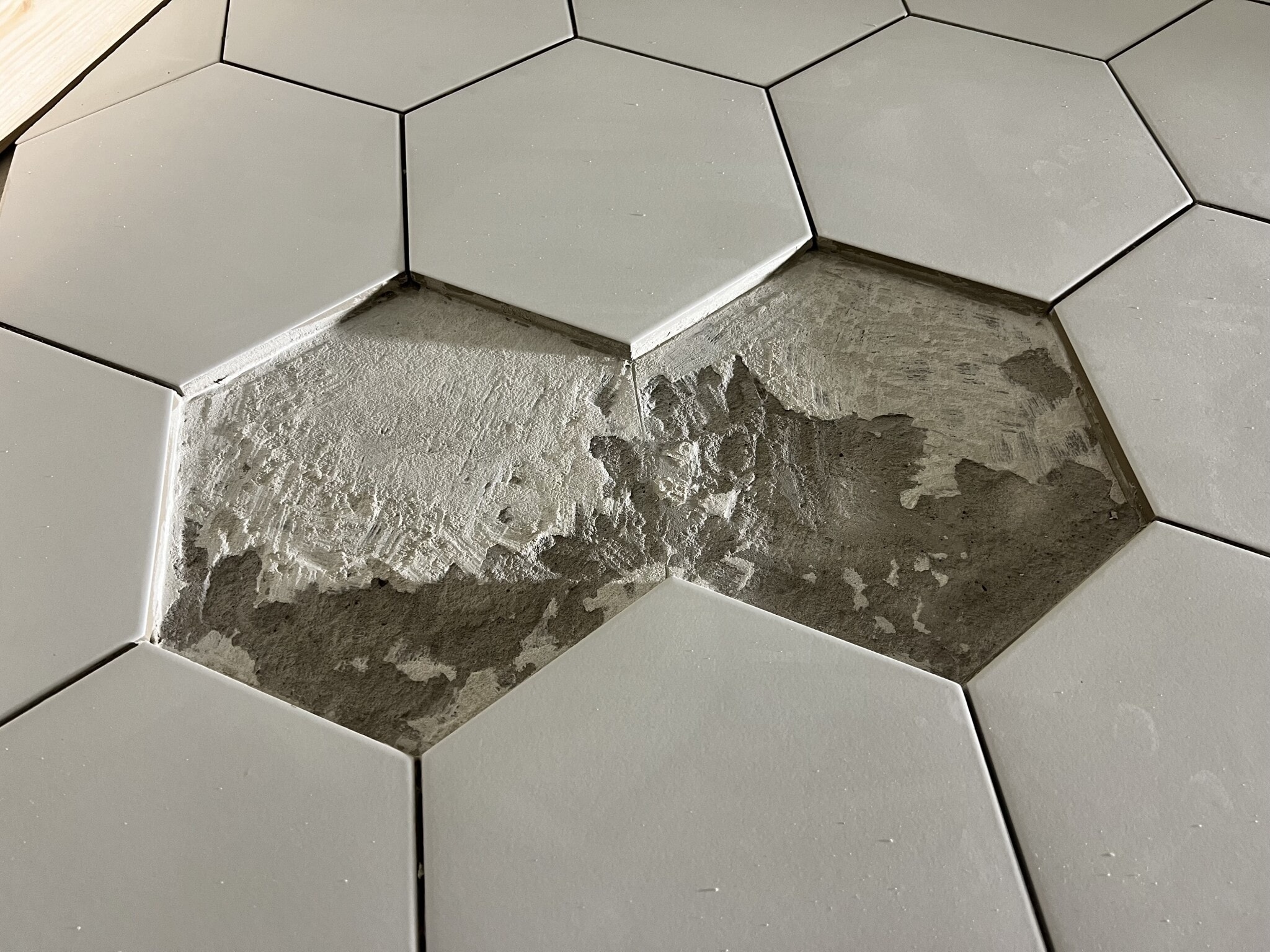 Grå hexagonala kakelplattor på golv, med ett saknat kakel avslöjande cementunderlag. Perfekt för modern renovering med geometrisk stil.