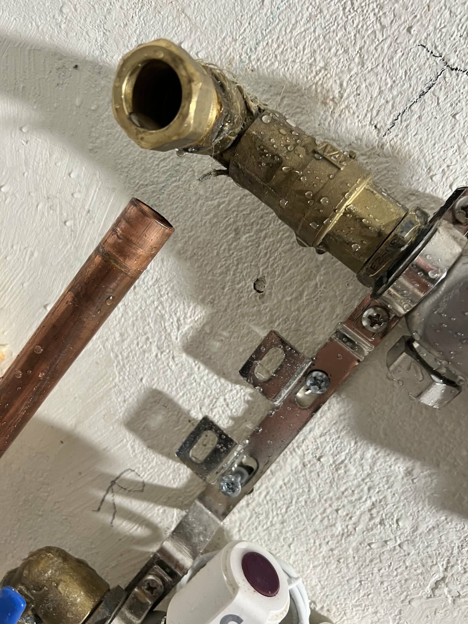 Närbild på en våt, koppar- och mässingsrörsanslutning mot en vit vägg, redo för reparation eller installation.